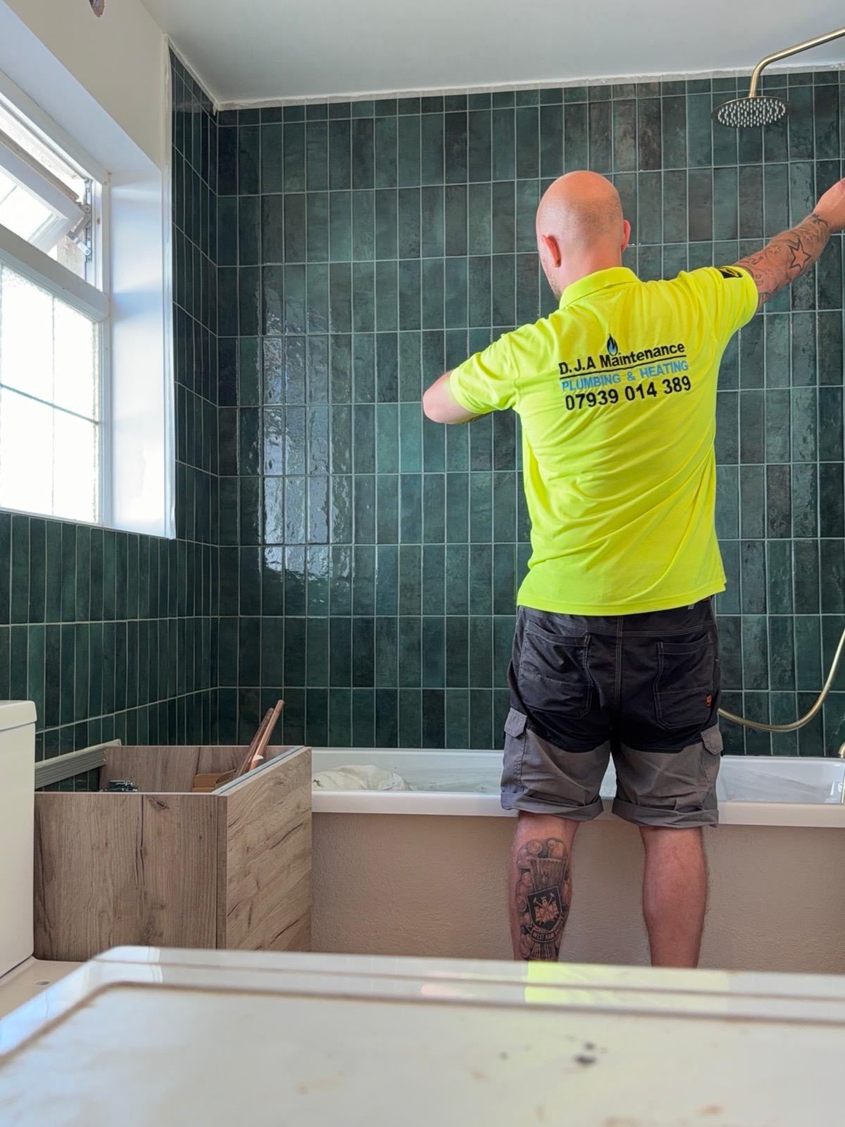 Fitting a rainfall shower over the bath in a green tiled bathroom